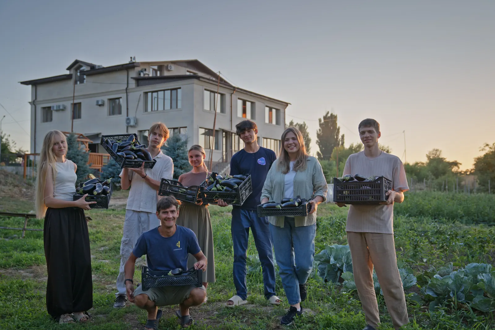 Students and staff holding crates of just-picked eggplant in front of the center at dusk